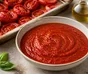 Ciotola di salsa di pomodoro rossa e liscia, circondata da pomodori arrostiti, aglio e basilico
