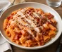 Rigatoni in salsa cremosa al pomodoro con pollo grigliato, bacon croccante e parmigiano grattugiato