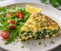 Frittata di spinaci e feta tagliata a spicchi accanto a rucola, pomodorini e prezzemolo riccio